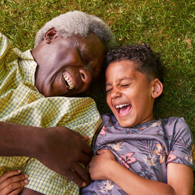 Laughing boy and grandfather lying on grass